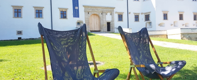 Zwei Sonnenstühle stehen im Schatten eines Baumes auf der Wiese vor Schloss Negova