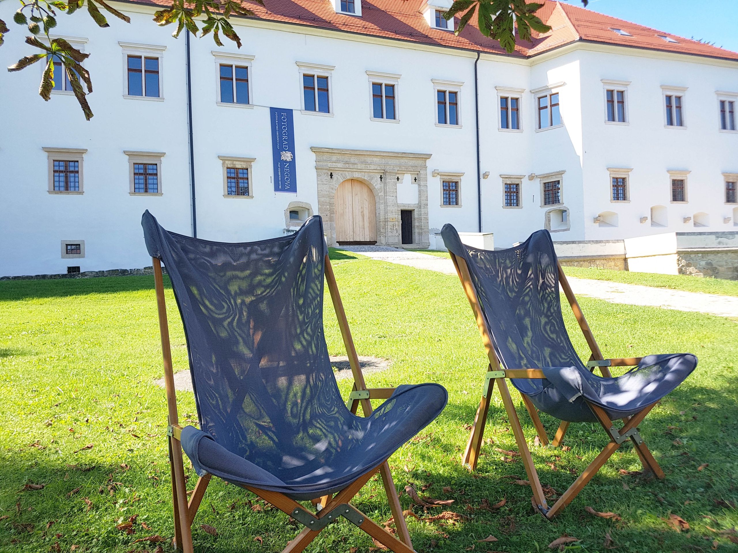 Zwei Sonnenstühle stehen im Schatten eines Baumes auf der Wiese vor Schloss Negova